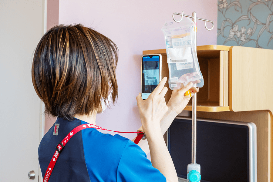スマホのカメラ機能で点滴の情報を撮影する看護師の写真
